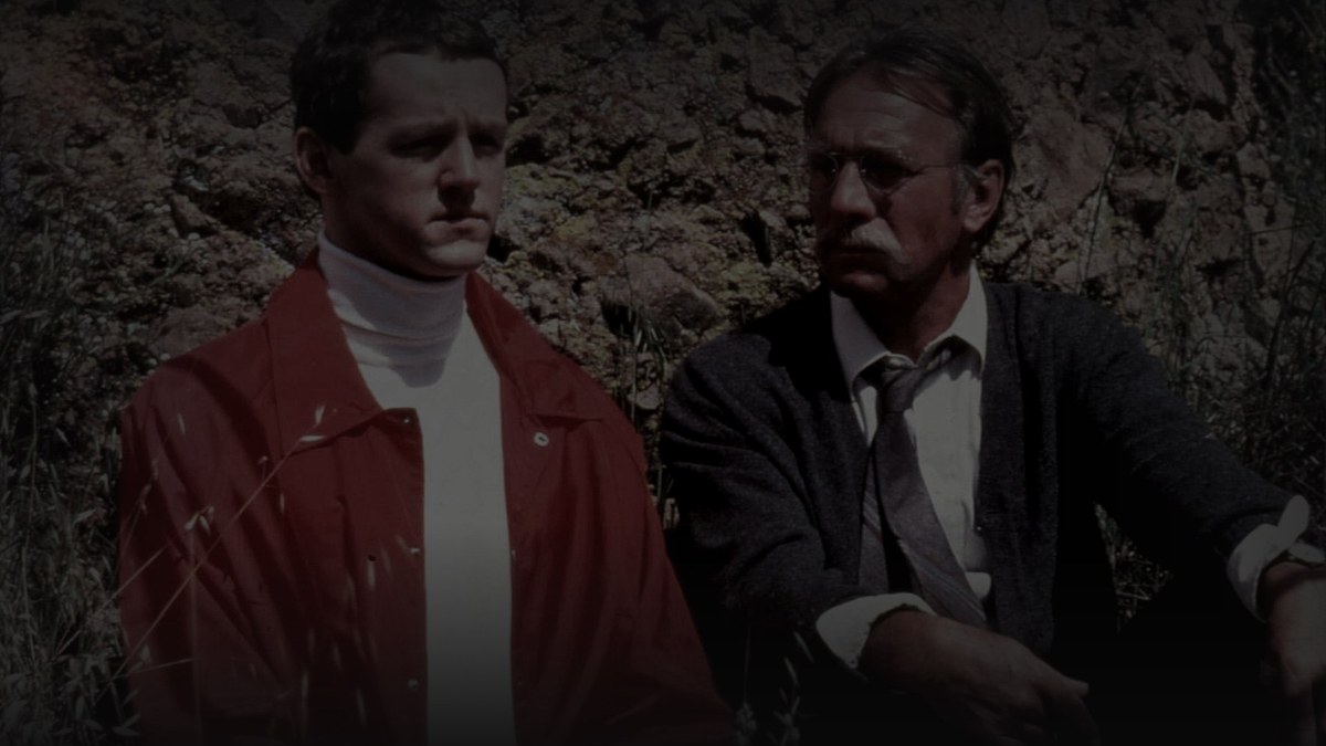 Still from Prototype (1983) — tmdb backdrop (id 53353); genuine film still of plummer and morse. pre-darkened source to 0.72 (source luma 103.4) and baked through scripts/bake_dark_photo.py at factor 0.45, 1200x675, on-disk luma 26.1